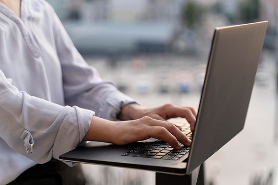 Person typing on a laptop outdoors while working remotely, with a blurred city background and modern professional setting.